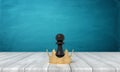 3d rendering of a small black chess pawn standing inside a golden crown on a wooden desk background.