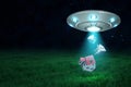 3d rendering of UFO above green field under night sky with three little houses falling down from its open hatch.