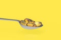 Vitamin Omega-3 fish oil capsules on metal spoon isolated on Yellow background