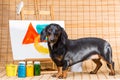 Dachshund artist near easel with its masterpiece