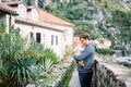 Dad with a baby in his arms stands near a stone fence in front of an old house at the foot of the mountains Royalty Free Stock Photo