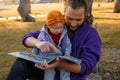 Dad and baby read a book under a tree in the park.