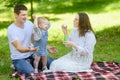 Dad and child are having fun, catching soap bubbles that mom blows while sitting on blanket in park on picnic. Summer Royalty Free Stock Photo