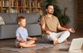 Dad with child little son doing yoga online, sitting in lotus pose on floor and meditating with closed eyes Royalty Free Stock Photo