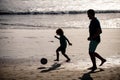 Dad and child playing outdoor, silhouette on sunset. Father and son play soccer or football on the beach on summer Royalty Free Stock Photo