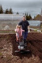 Dad and daughter cultivate the ground in the garden with a walk-behind.