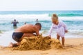 Dad and daughter make sand castle on the shore of a sandy tropical beach in the background of bathing people Royalty Free Stock Photo