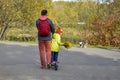 Dad drives his daughter on a scooter on a track in the park in the fall.