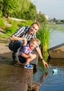 Dad helps the Little Boy to lower the paper boat to the water in Royalty Free Stock Photo