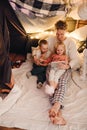 Dad and his kids watching cartoons on tablet while sitting in handmade tent in children's room