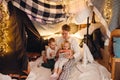 Dad and his kids watching cartoons on tablet while sitting in handmade tent in children's room
