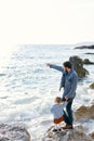Dad is holding a little girl by the hand, standing with her on a large stone by the water and pointing to the sea with Royalty Free Stock Photo