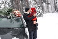 Dad holds his little daughter, kissing her and gently hugging her in the woods next to the car and the Christmas tree. Royalty Free Stock Photo