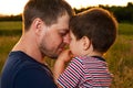 Dad holds his young son in his arms and hugs him in a summer field at sunset in the evening. Dad`s love, attachment to the child. Royalty Free Stock Photo