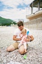 Dad holds little girl on his lap while sitting on pebble beach