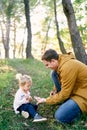 Dad holds out a tiny mushroom in the palm to a little girl sitting in the forest on the grass Royalty Free Stock Photo