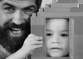 Dad and kid hide behind house made of plastic blocks. Boy and man play together, close up. Father and son Royalty Free Stock Photo