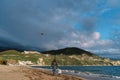 Dad and little daughter are walking along the seashore with a soaring kite. Back view