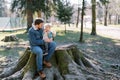 Dad with a little girl on his knees sits on a huge stump in a sunny spring park