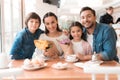 Dad and the little son are giving flowers to mother and daughter in a cafe. Royalty Free Stock Photo