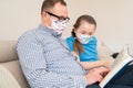 Dad in medical mask on his face reads book with child.