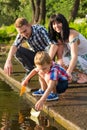 Mom, dad and their little son launch paper boats in a river in t