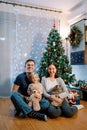 Dad and mom are sitting near the Christmas tree with a little girl and a cat on their laps Royalty Free Stock Photo