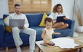 Dad and mom sitting on sofa with computer while daughter painting in living room. Young parent using laptop for works and little