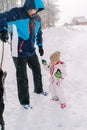 Dad plays with black dog with stick while standing with little girl on snowy road Royalty Free Stock Photo