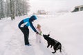 Dad plays with a black dog with a stick while standing with a little girl on a snowy village road Royalty Free Stock Photo