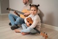 Dad plays the guitar with his daughter. The child learns to play a musical instrument with a tutor. Musical duet of a