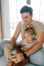 Dad plays with a little girl with a teddy bear sitting with her on the bed Royalty Free Stock Photo