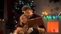 Dad reading book for adorable daughter near Christmas tree, magic atmosphere