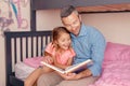 Dad reading book to daughter girl. Happy family of two sitting on bed in bedroom. Smiling father and child at home spending time Royalty Free Stock Photo