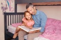 Dad reading book to pre-teen daughter girl. Happy family of two sitting on a bed in bedroom. Smiling father and child at home Royalty Free Stock Photo
