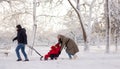 Dad rolls his three-year-old daughter in a sleigh through the snow in a winter park between the trees, while Mom pushes Royalty Free Stock Photo