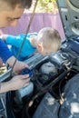 Dad shows his son where to fill in the coolant in the engine compartment. Topping up antifreeze in the car cooling system. Royalty Free Stock Photo