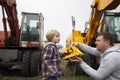 Dad and son, against background of construction equipment - excavators, are enthusiastically examining a toy bulldozer Royalty Free Stock Photo