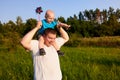 Dad and son having fun in nature in summer, father holding his child on his shoulders with pinwheel