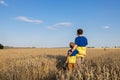 dad and son in identical yellow blue t-shirts stand embracing in wheat field