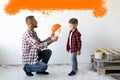 Dad and son are renovating a room in the house. A man puts on a helmet for his son against a white wall with an orange Royalty Free Stock Photo