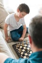 Dad and son are sitting on the couch and playing chess. Leisure with children, pastime and games