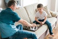 Dad and son are sitting on the couch and playing chess. Leisure with children, pastime and games