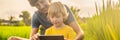 Dad and son sitting on the field holding tablet. Boy sitting on the grass on sunny day. Home schooling or playing a Royalty Free Stock Photo