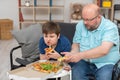 Dad and son are sitting on the sofa in the room eating pizza. Royalty Free Stock Photo