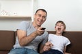 Dad and son are watching TV and laughing loud. Family friendly relations