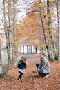 Dad squats in the autumn forest throwing fallen leaves at a little jumping girl. Side view