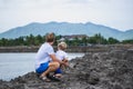 Dad squatting hugging son, holding hands together near lake looking far away. Happy childhood, fatherhood. Family