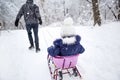 Dad takes his little daughter on a sledge uphill through the winter snow forest. Active family outdoor