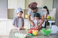 Dad teaches girl hot to cut tomatos. He helps her. Boy looks at it. He is concentrated. Woman stands behind them and